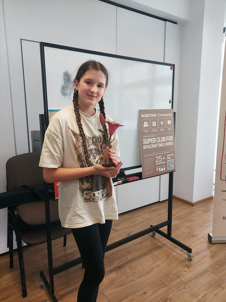 Mariia holds her flower model beside the Robotime meetup sign in Warsaw