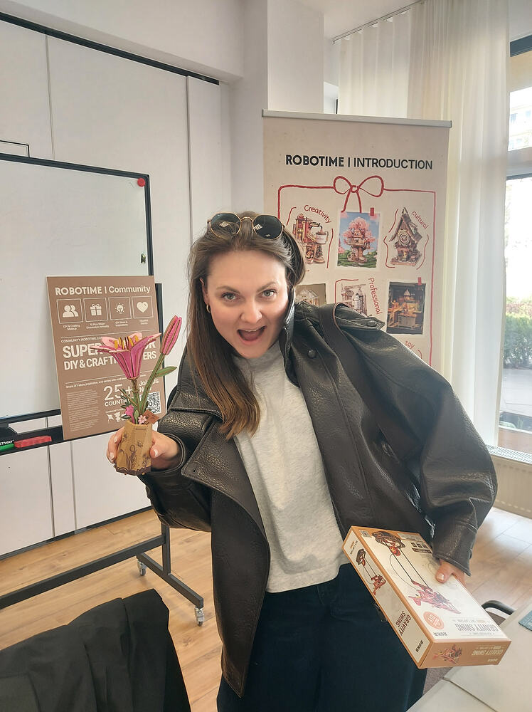Een lachende deelnemer houdt een voltooid houten bloemenmodel en de doos van de Robotime-kit vast