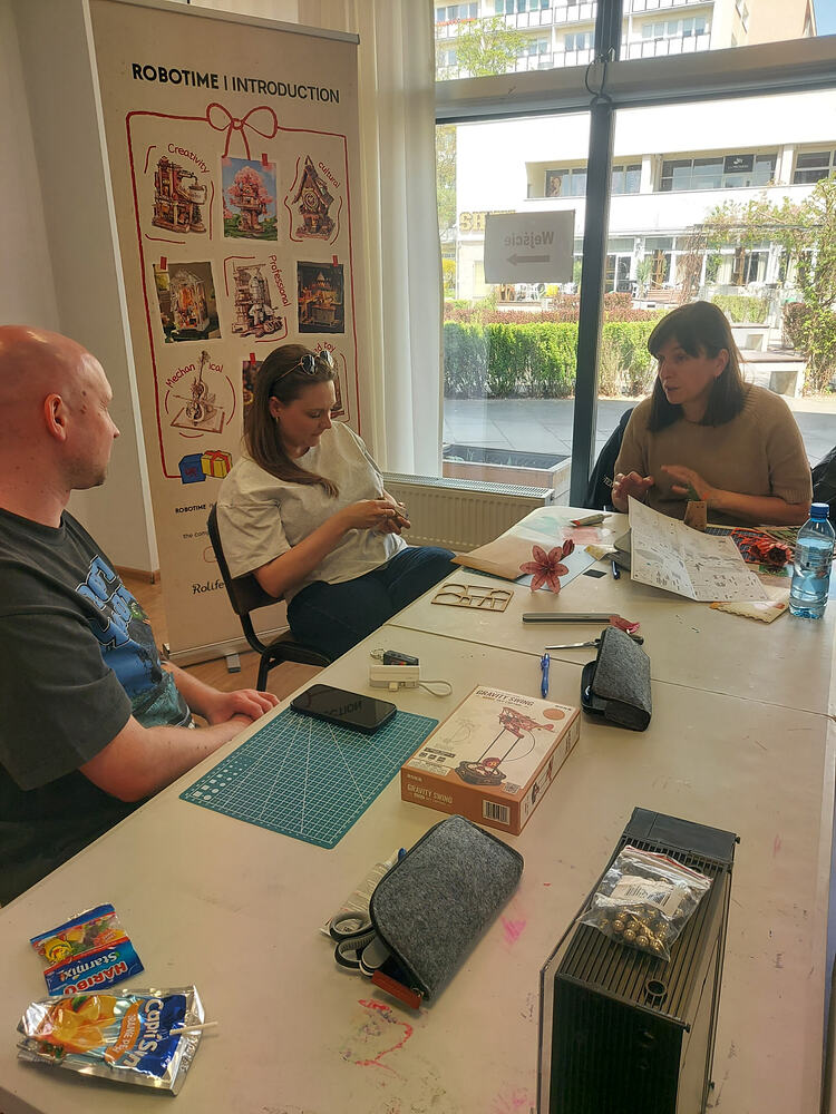 Three Warsaw meetup participants talk while working on flower and wooden model pieces