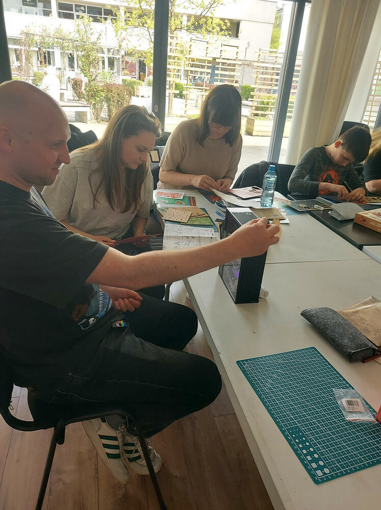 Volwassenen en kinderen werken zij aan zij aan Robotime-kits naast de ramen van de locatie