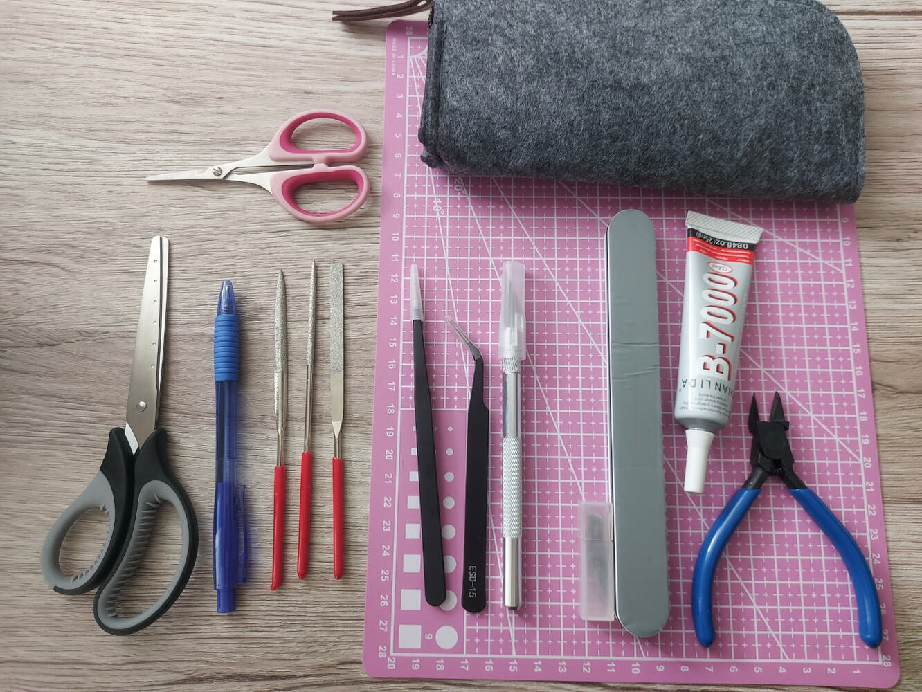 Scissors, tweezers, files, a craft knife, glue, pliers, and a cutting mat arranged as a participant toolkit