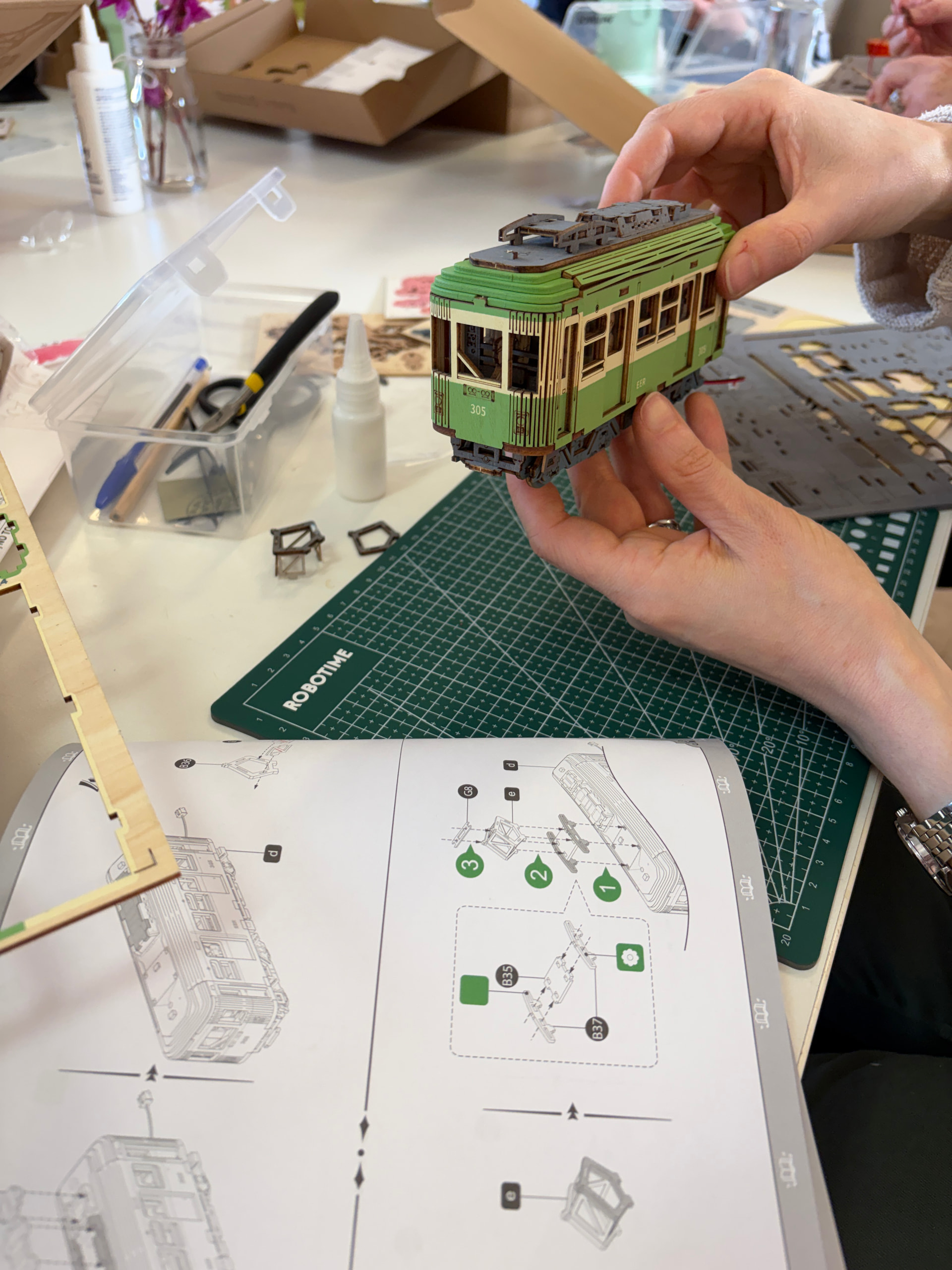 Ein Teilnehmer hält eine teilweise montierte grüne Miniatur-Straßenbahn über ihre Anleitung