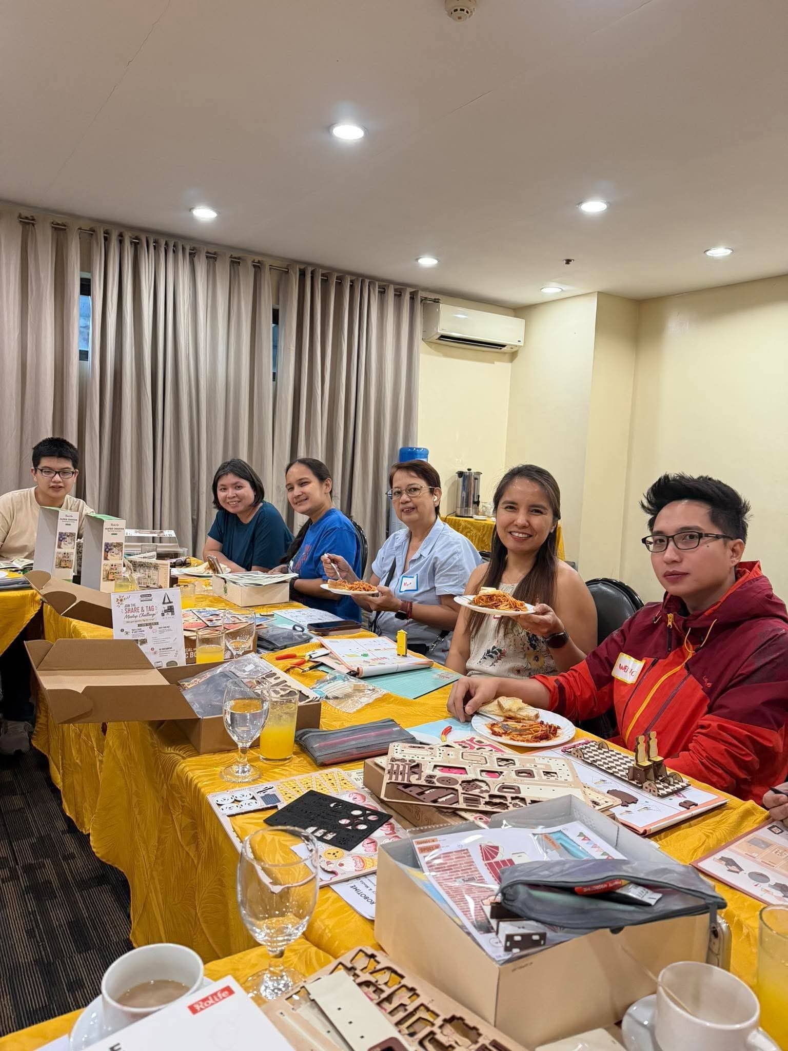 Participants souriant au-dessus de feuilles de kits en bois ouverts et de collations sur une table partagée