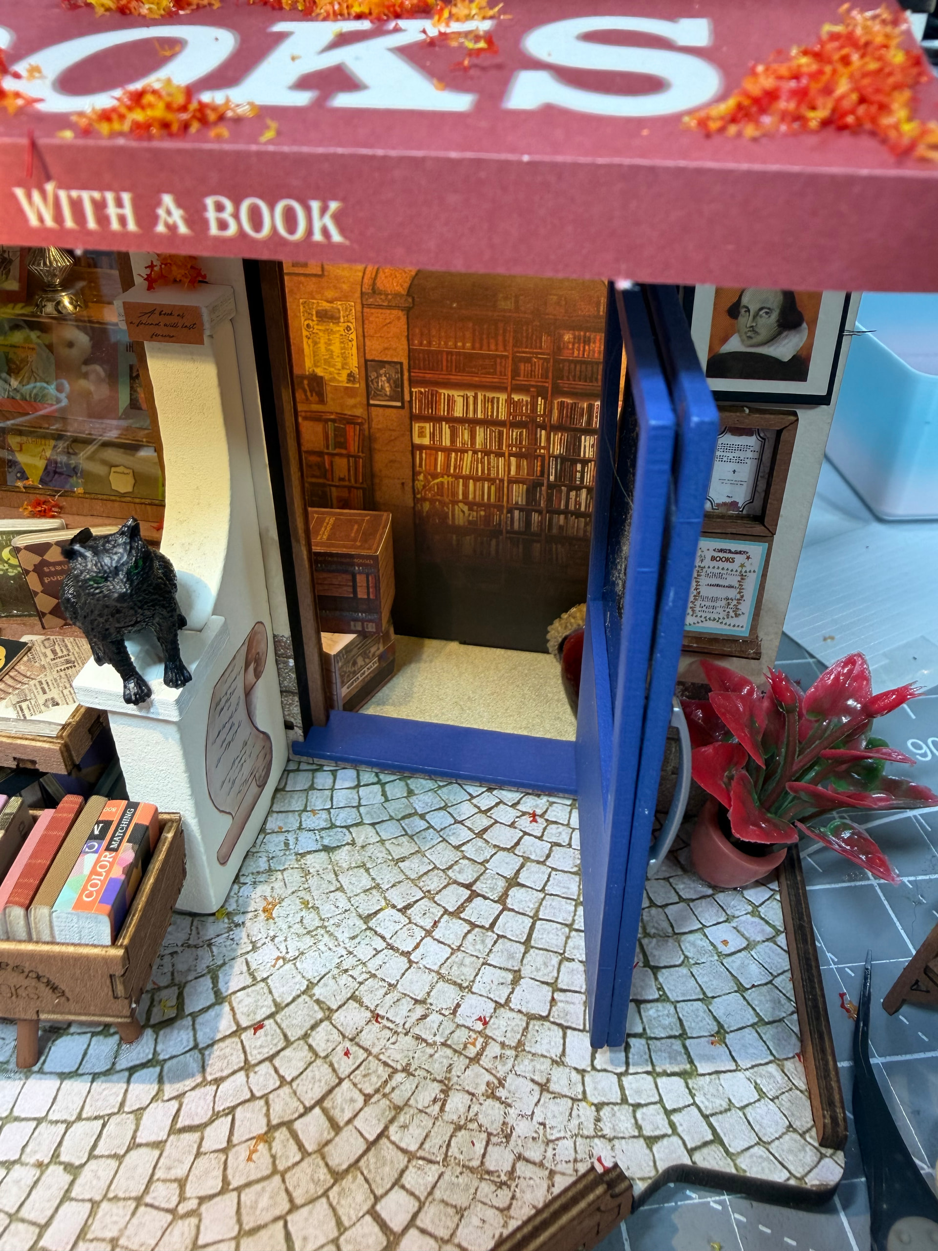 Die blaue Buchhandlungstür öffnet sich zu den inneren Regalen, mit einer schwarzen Katze und verstreuten Büchern im Vordergrund