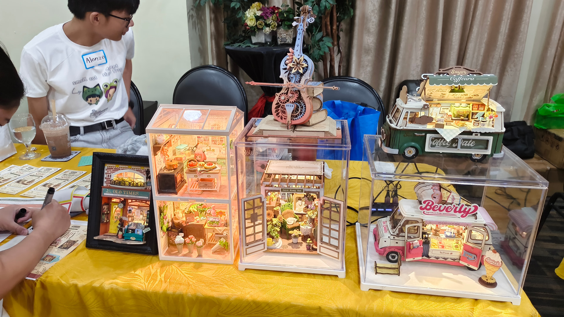 Une table d'exposition remplie de boutiques miniatures illuminées, d'une boîte à musique et de modèles de camions de nourriture